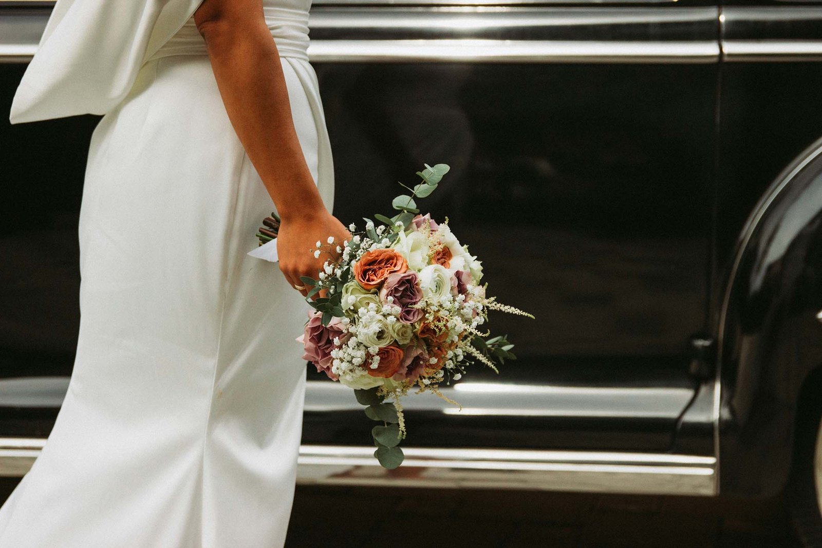 Bride holding her bouquet beside a vintage car